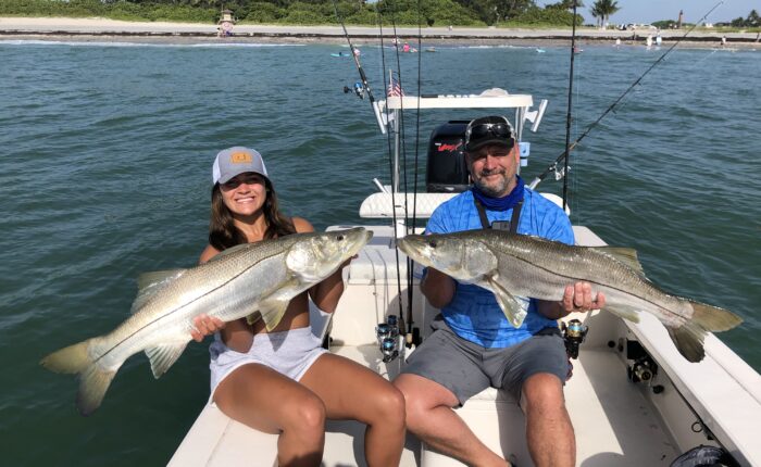 Two people on a Snook Fishing Charter holding up two large striped bass.