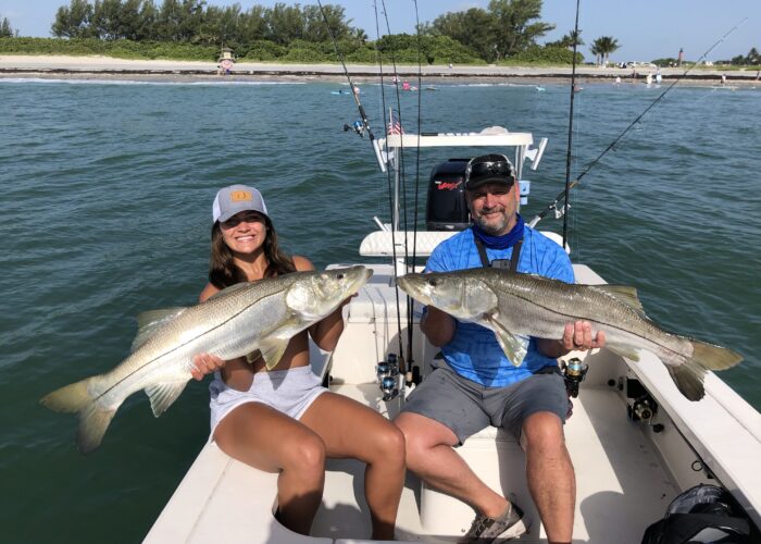 Two people on a Snook Fishing Charter holding up two large striped bass.